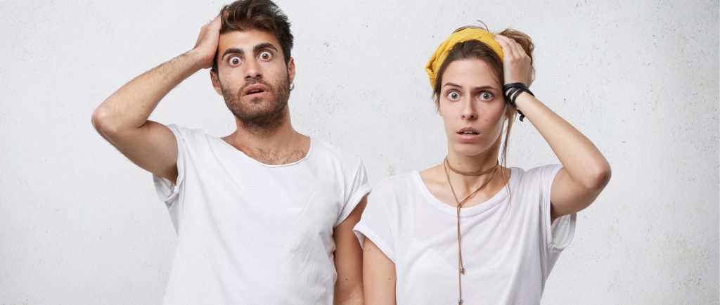 גבר ואישה צעירים מביטים קדימה בעיניים פעורות, כשיד אחת מונחת על ראשם בהבעת הלם ובלבול המחשה של תגובה רגשית למצבים לא צפויים, טעות או שוק מיידי.